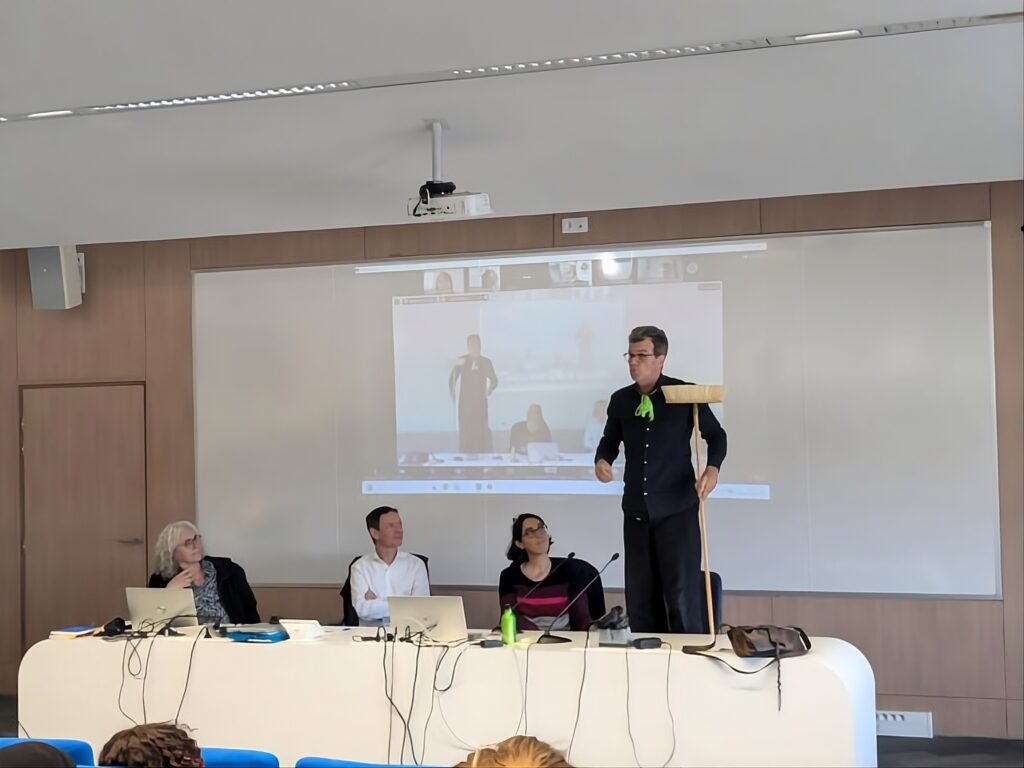 Conférence créative philippe-sahuc en France, orateur sur la table avec balai et public devant un écran projeté